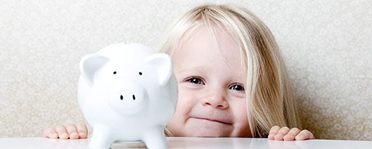 A little, blonde haired girl smirking next to her white piggy bank