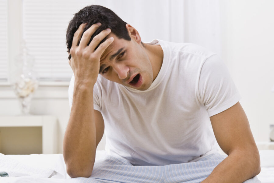 Brunette white man in his pajamas yawns after waking up from poor quality sleep due to obstructive sleep apnea