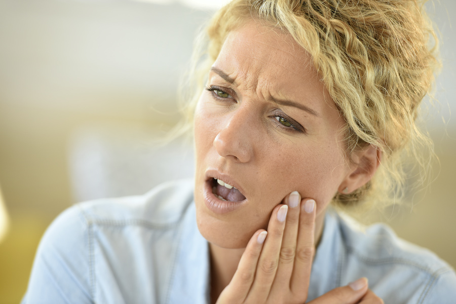 Blonde woman touches her cheek because she is experiencing pain from dry socket after a tooth extraction