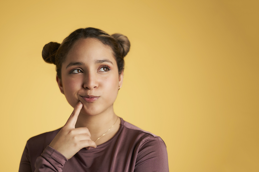 Brunette young woman touches her lips and looks up wondering against a yellow background