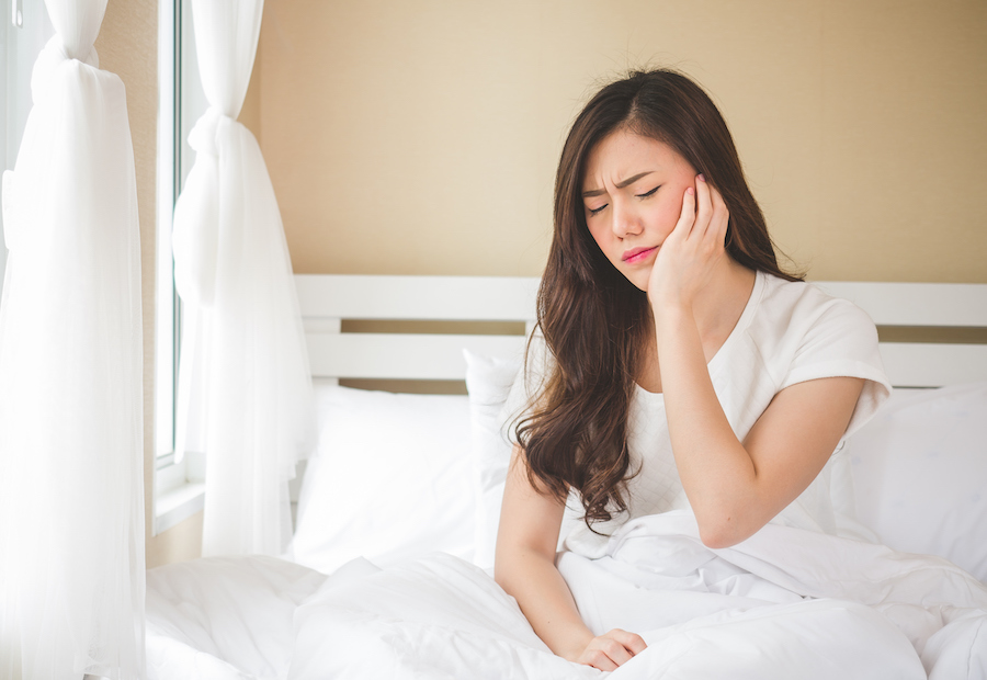 Brunette woman cringes in pain and touches her cheek and ear due to an earache