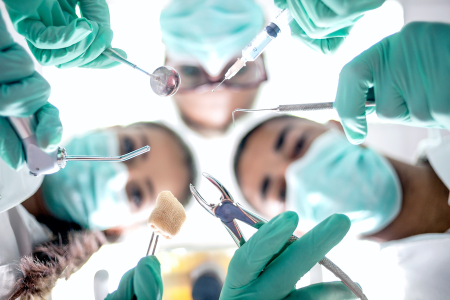 Looking up into 3 dental professionals in teal scrubs holding oral surgery tools